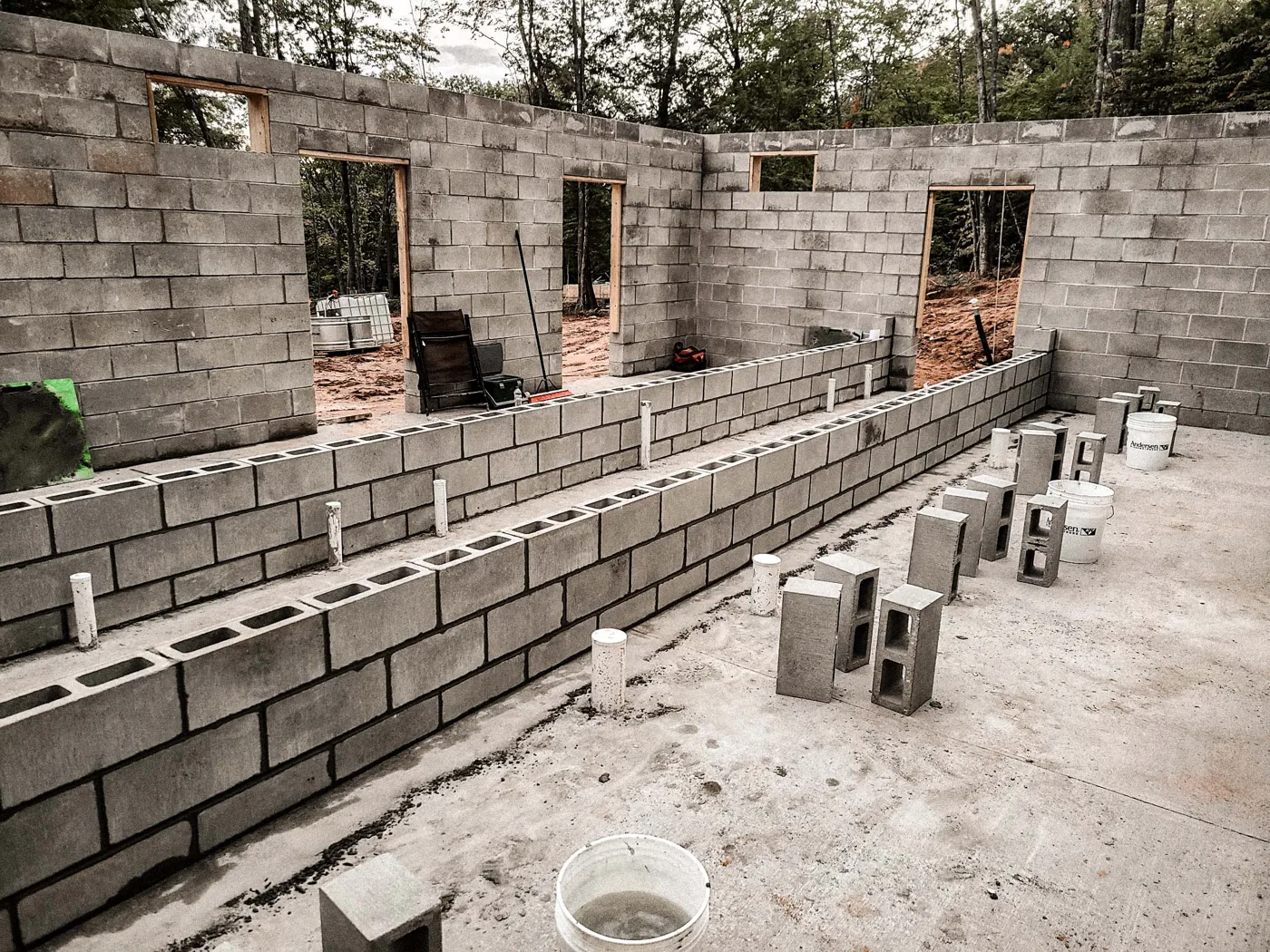 Concrete block walls with door and window openings, loose blocks and buckets on the slab