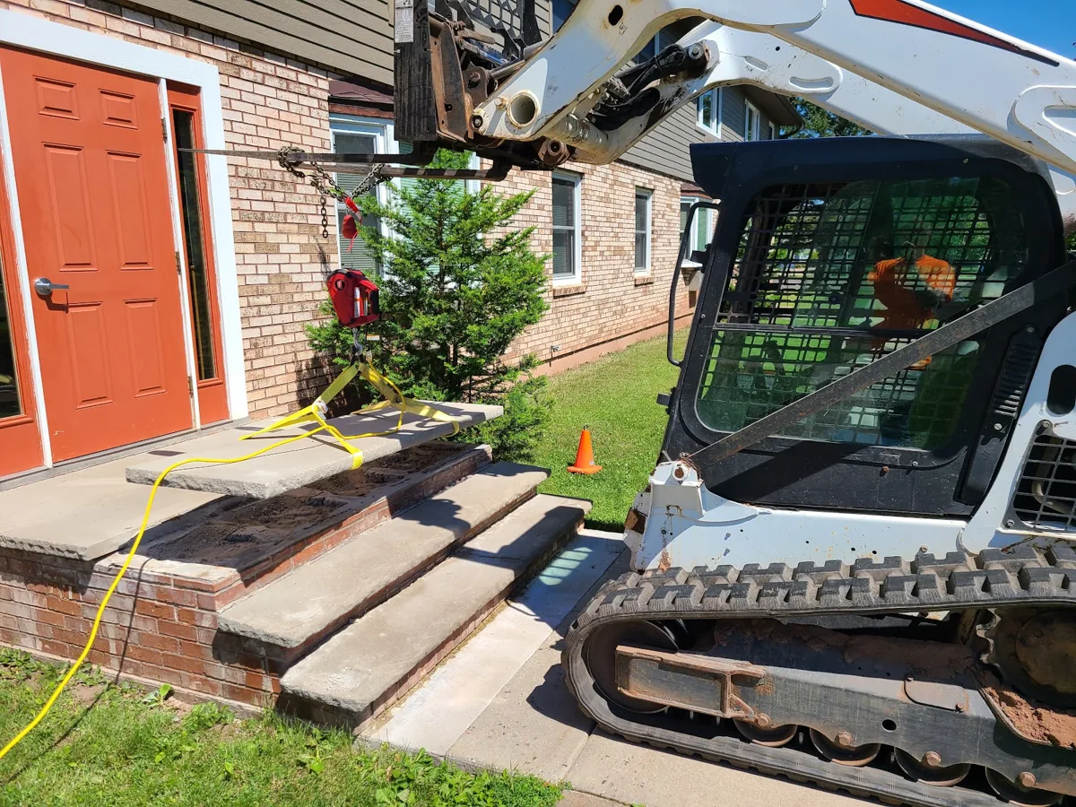 Lifting equipment holding a stone tread above brick entrance steps beside an orange door