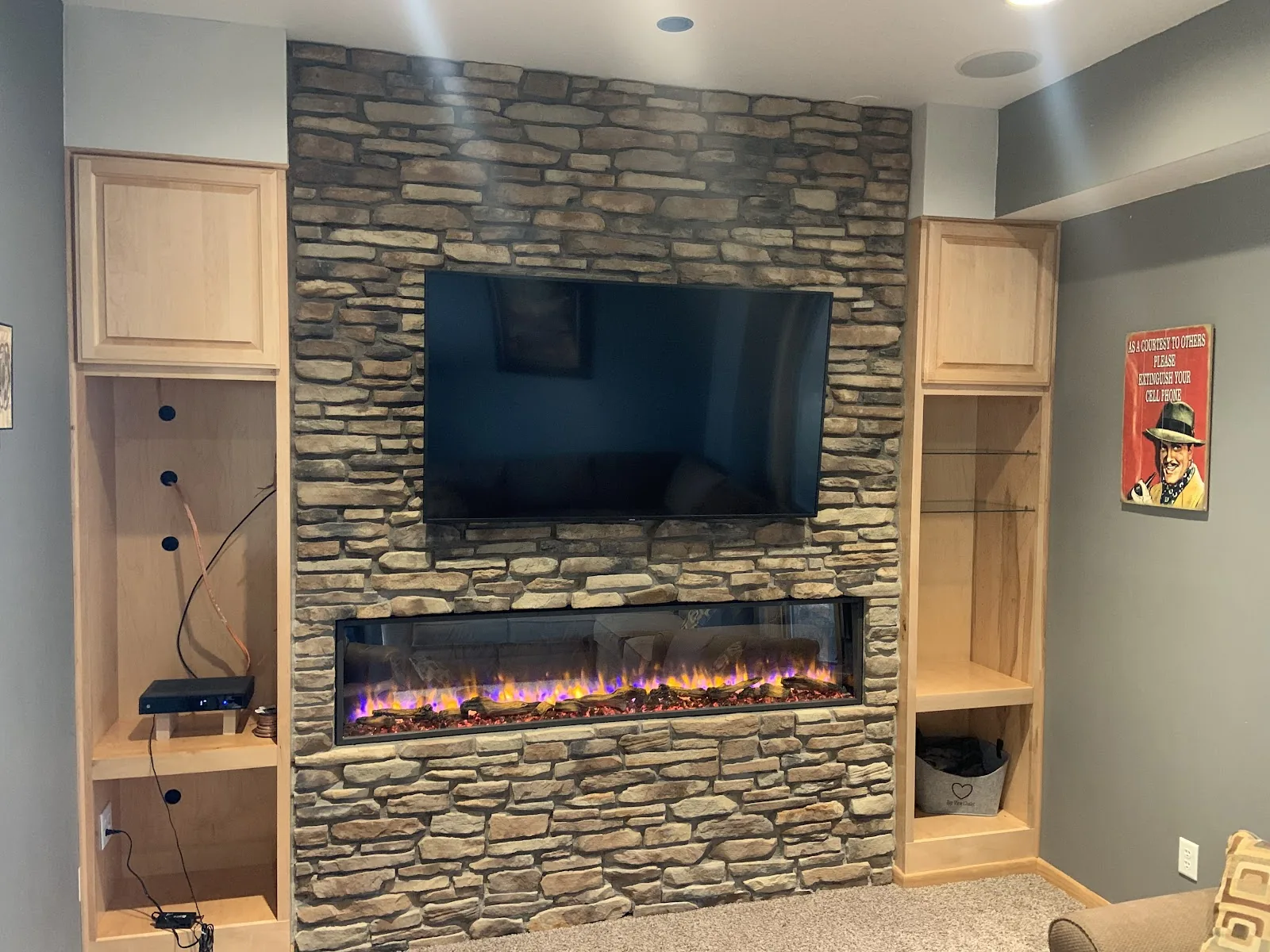 Ledgestone wall around a long fireplace, with a television above and wood cabinets at each side
