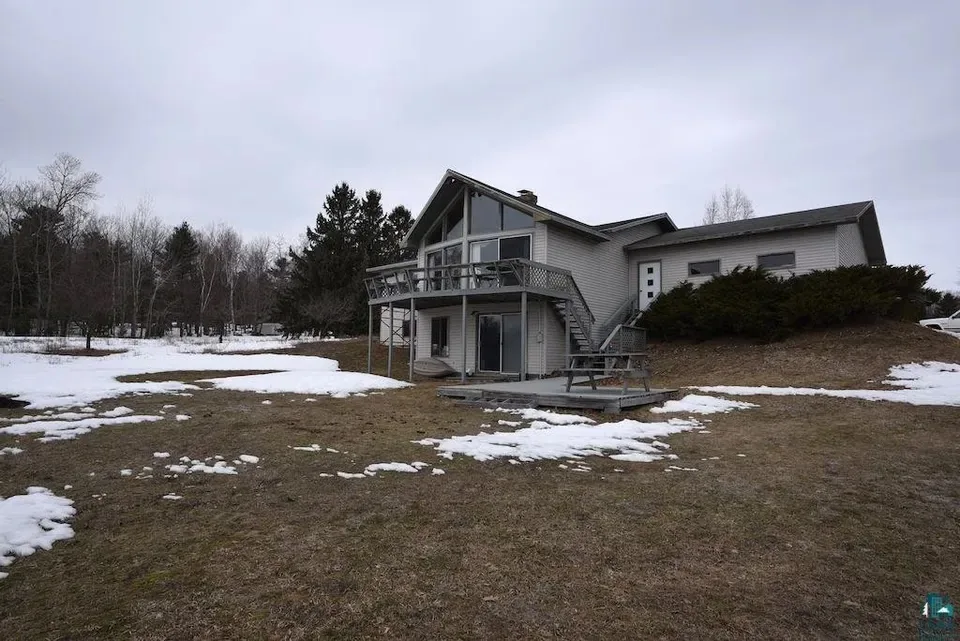 A gray house with a deck, surrounded by snow and bare trees